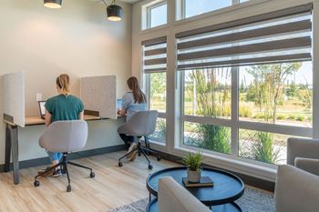 Two women are working at computers in a room with large windows.